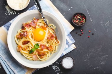 Geleneksel İtalyan makarna yemek, spagetti carbonara sarısı, parmesan peyniri, pastırma plaka siyah rustik taş zemin, üstten görünüm, metin için yer. İtalyan yemek makarna ile 