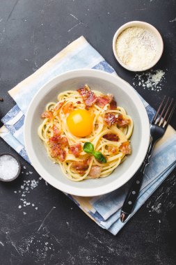 Geleneksel İtalyan makarna yemeği, yumurtalı spagetti carbonara, parmesan peyniri, siyah taştan arka planda pastırma, üst manzara. İtalyan yemeği ve makarna. 