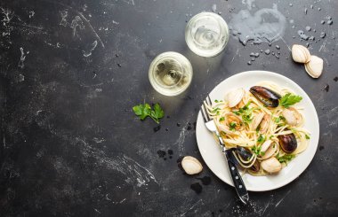 Spagetti vongole, istiridye ve midye otlar ile plaka ile İtalyan Deniz ürünleri makarna ve iki bardak beyaz şarap rustik taş arka plan, metin için yer. İtalyan Deniz mutfağı, yakın çekim, üstten görünüm