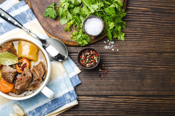 Close-up of slow cooked meat stew ragout in bowl with beef, potato, carrot, broth on wooden rustic background, top view with space for text. Hot homemade food for dinner, meat casserole copy spac