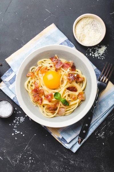 Traditional Italian pasta dish, spaghetti carbonara with yolk, parmesan cheese, bacon in plate on black rustic stone background, top view. Italian dinner with pasta