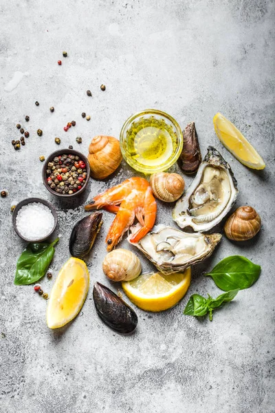 Assortment of fresh seafood: oysters, shrimps, clams, mussels, shells with lemon, olive oil, herbs on grey stone rustic background, top view. Ready for cooking seafood, close-up