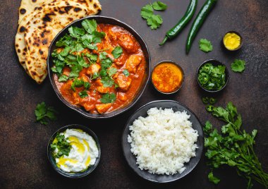 Geleneksel Hint yemeği tavuk tikka masala baharatlı Körili et kase, basmati pirinç, ekmek naan, yoğurt raita sos üstten görünüm, rustik koyu arka plan üzerinde yakın çekim. Hint tarzı yemek yukarıdan 