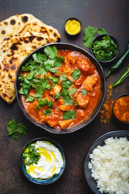 Geleneksel Hint yemeği tavuk tikka masala baharatlı Körili et kase, basmati pirinç, ekmek naan, yoğurt raita sos üstten görünüm, rustik koyu arka plan üzerinde yakın çekim. Hint tarzı yemek yukarıdan 