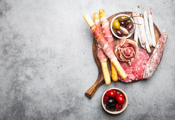 Variety of cold meat cuts and appetizers, prosciutto, jamon, salami slices, sausage, grissini, olives. Assorted mix of meat on rustic wooden board, space for text, top view, close-u