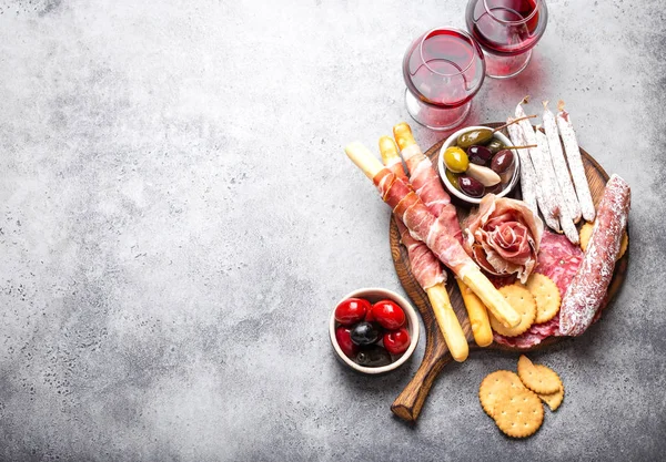 Variety of cold meat cuts and appetizers, red wine, prosciutto, jamon, salami slices, sausage, grissini, olives. Assorted mix of meat on rustic wooden board, space for text, top view, close-u