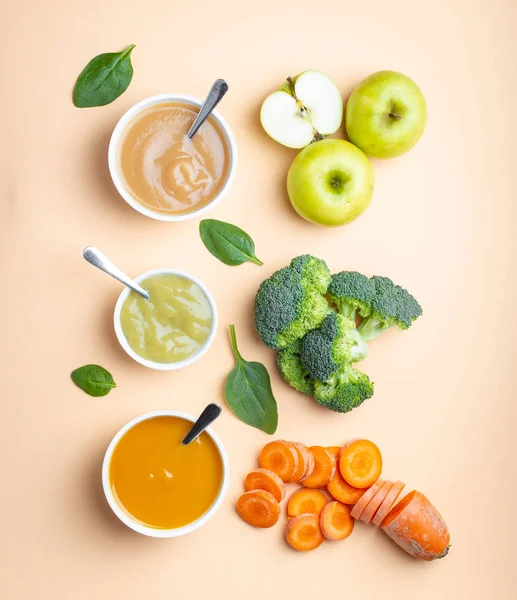 White bowls with healthy natural baby food on pastel background. Purees, made of fresh organic fruit and vegetables, flay lay, top view, concept. Kids food made from carrot, broccoli, apples, spinach