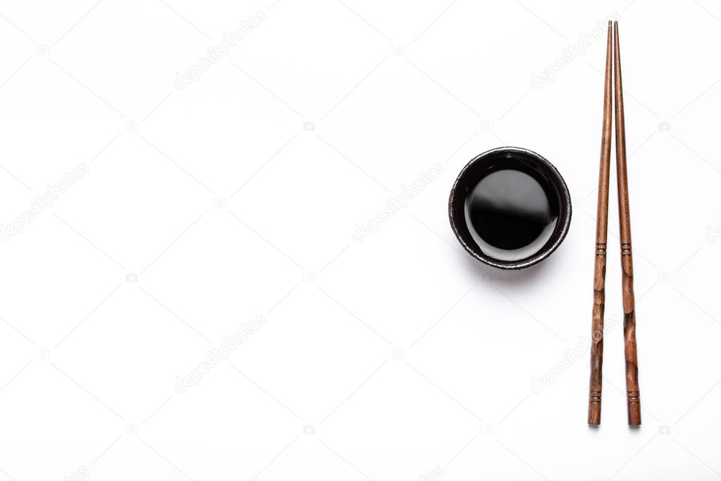 Little rustic bowl with soy sauce and wooden chopsticks over white background with space for text. Concept of sushi restaurant, Japanese cuisine or menu template, top view 