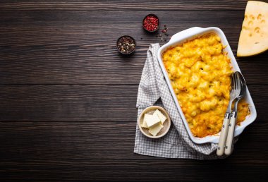 Fırında makarna ve peynir çeşnilikler tereyağı, metin için kaşık ve çatal, üstten görünüm, yer ile ahşap arka plan üzerinde beyaz güveç içinde Close-up. Peynirli soslu makarna, İngilizce/gıda konfor.