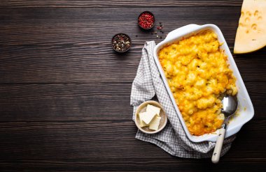 Fırında makarna ve peynir çeşnilikler tereyağı, metin için kaşık ve çatal, üstten görünüm, yer ile ahşap arka plan üzerinde beyaz güveç içinde Close-up. Peynirli soslu makarna, İngilizce/gıda konfor.