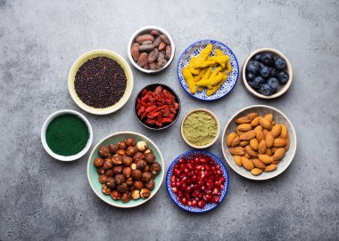 Kase taş gri arka plan üzerinde farklı superfoods kümesi: spirulina, goji berry, kakao, matcha yeşil çay tozu, quinoa, chia tohumu, yaban mersini, mutlu sağlıklı yaşam için fındık, ana sayfa görünümü, yakın çekim