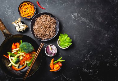 Tavada kızartılmış erişte soba yapmak için malzemeler. Wok tavada taze sebze kesme, haşlanmış soba yemek, siyah taş arka plan, metin, en iyi görünüm için yer için hazır yemek çubukları ile kase erişte