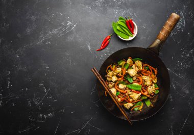 Fry tavuk eski rustik wok tavada sebze, yemek çubukları ile siyah taş zemin üzerine ilave edin, yakın çekim, görünümü top. Geleneksel Asya/Tay yemek, metin için yer