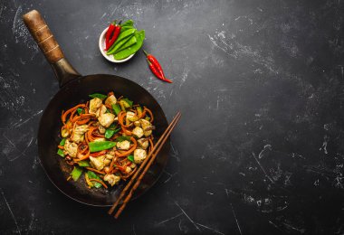 Fry tavuk eski rustik wok tavada sebze, yemek çubukları ile siyah taş zemin üzerine ilave edin, yakın çekim, görünümü top. Geleneksel Asya/Tay yemek, metin için yer
