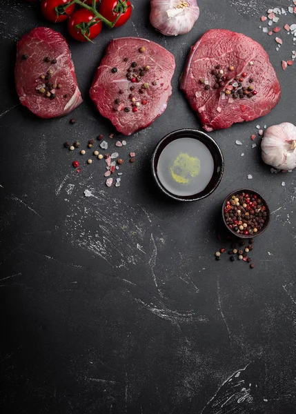 Close-up of raw fresh marbled meat steak on dark rustic concrete background with salt and pepper, olive oil, garlic ready ti be cooked. Cooking meat concept with space for text, top view