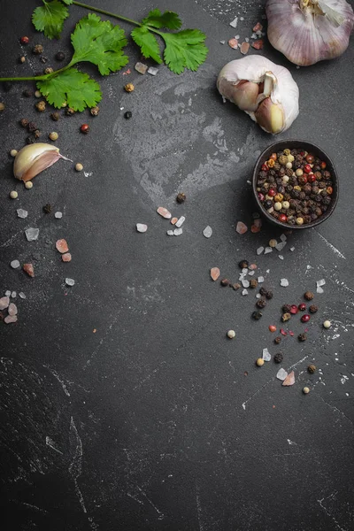 Close up of traditional cooking ingredients: garlic, olive oil, salt, pepper, fresh herbs on dark rustic background. Food frame, concept for cooking healthy food with space for text, top view