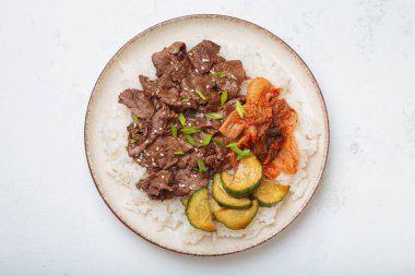 Pirinçli bulgogi kasesi, kavrulmuş et dilimleri, kimchi ve salatalık ezmesi beyaz arka plan manzaralı, geleneksel Kore yemeği.