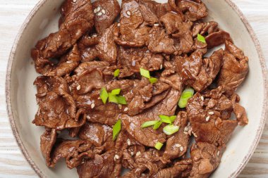 Kore 'nin geleneksel yemeği Bulgogi' nin kavrulmuş sığır eti dilimlerinin yakınında susam tohumları ve taze soğanlarla süslenmiş, hafif ahşap masa manzaralı geleneksel kimchi ile servis edilir.