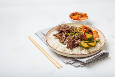 Pirinçli bulgogi kasesi, kavrulmuş et dilimleri, kimchi ve salatalık ezmesi beyaz arka planda, geleneksel Kore yemeği, kopyalama alanı.