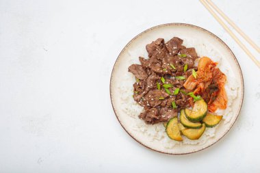 Pirinçli bulgogi kasesi, kavrulmuş et dilimleri, turşu ve soslu salatalık beyaz arka plan manzaralı, geleneksel Kore yemeği, kopyalama alanı.