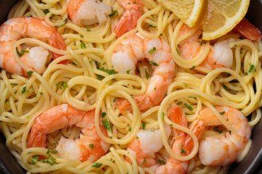 Siyah dökme demir tavada servis edilen dhrimps makarna spagettisi taze limon dilimleri ve siyah kırsal arka planda maydanoz üst görünümü ile süslenmiş