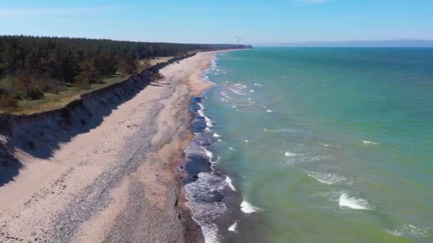 Widok z lotu ptaka wzdłuż łotewskiego wybrzeża nadbałtyckiego plaży w kierunku turbiny wiatrowej w pobliżu Liepaja — Wideo stockowe