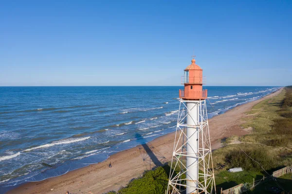 Aerial view of lighthouse with red top and white base. Blue sky and sea. Pape lighthouse