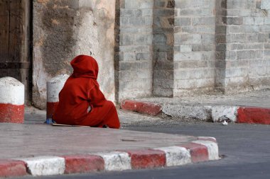 Marakeş, Fas - 14 Mayıs 2013: Kırmızı ve beyaz kaldırımda oturan kırmızı elbiseli bir kadın.