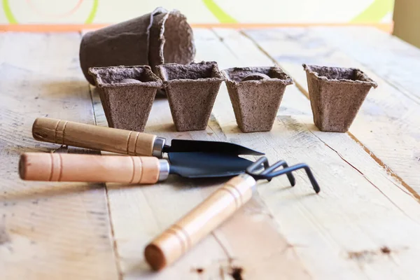 Tahta arka planda biyolojik çözünür çömlek, tırmık ve kürek. Bahçe araçları.