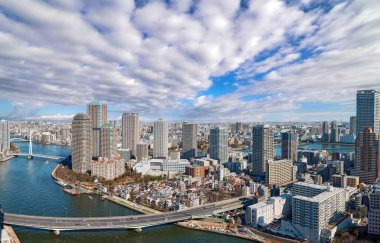 Tokyo 'daki Sumida nehrinin geniş açılı hava manzarası dalgalı su, tekne, köprü ve dramatik gökdelenler altında