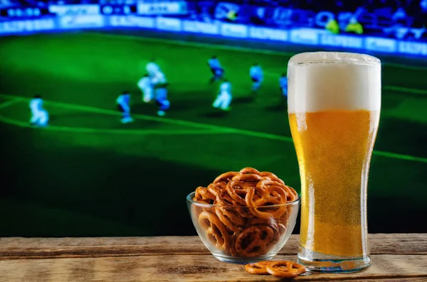 Glass of beer and snack on a football game TV background