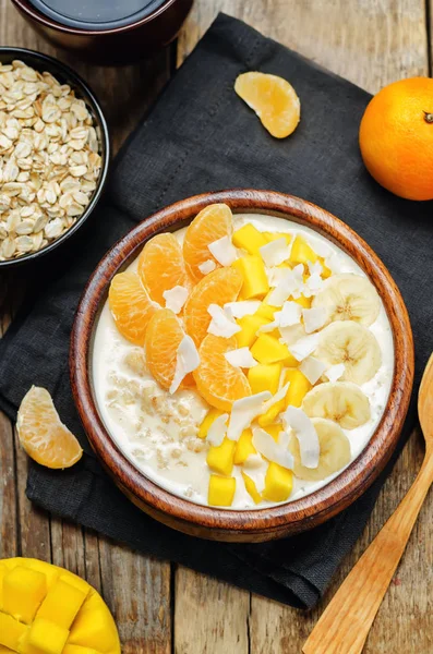 Oatmeal with mango, banana, tangerine oranges and coconut flakes. toning. selective focus