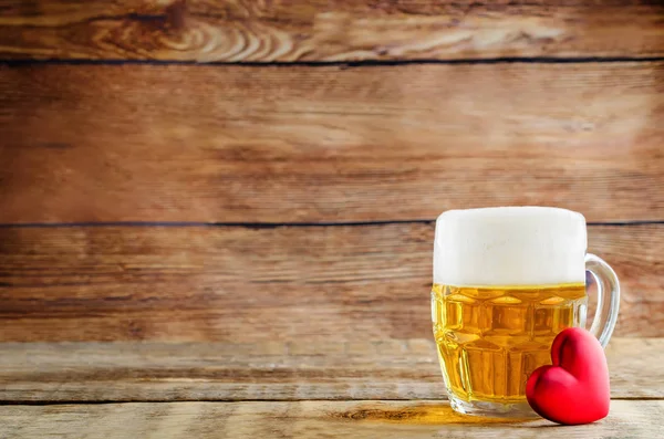 Glass of cold light beer with heart on a wood background for Val