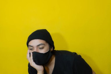 Cesareti kırılmış ya da sıkılmış çenesinde çene kemeri olan elini tutup aşağıya bakan genç bir adam.