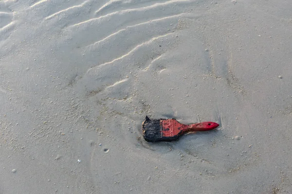 Old red paint brush on sand