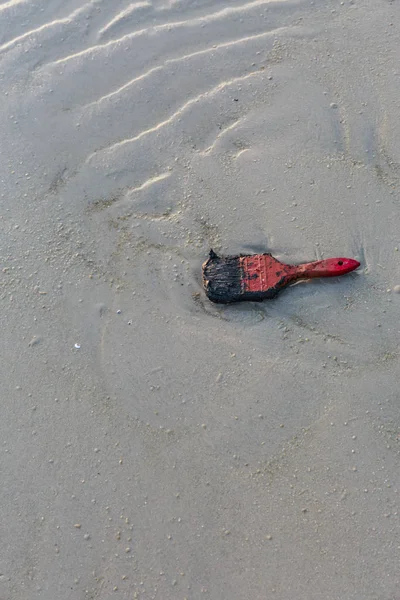 Old red paint brush on sand