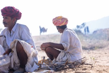 Puşkar, Rajasthan, Hindistan - 10 Kasım 2024: Geleneksel beyaz giysili rajasthani erkek portresi çöl panayırında renkli türbanlı deve fuarı sırasında develeri takas etmek için.