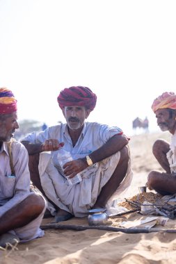 Puşkar, Rajasthan, Hindistan - 10 Kasım 2024: Geleneksel beyaz giysili rajasthani erkek portresi çöl panayırında renkli türbanlı deve fuarı sırasında develeri takas etmek için.