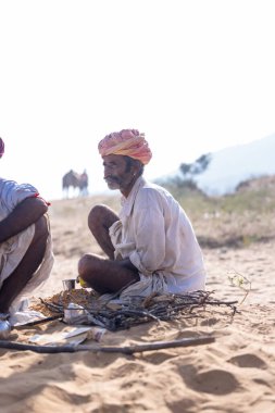Puşkar, Rajasthan, Hindistan - 10 Kasım 2024: Geleneksel beyaz giysili rajasthani erkek portresi çöl panayırında renkli türbanlı deve fuarı sırasında develeri takas etmek için.