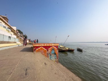 Varanasi, Uttar Pradesh, Hindistan - 18 Kasım 2022: Varanasi 'deki nehir çetelerinin yakınlarındaki ghatlarda kimliği belirsiz insanlarla antik binaların ve tapınakların mimari görünümü.