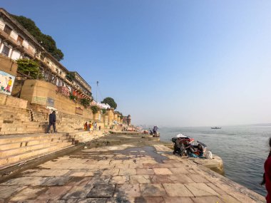 Varanasi, Uttar Pradesh, Hindistan - 18 Kasım 2022: Varanasi 'deki nehir çetelerinin yakınlarındaki ghatlarda kimliği belirsiz insanlarla antik binaların ve tapınakların mimari görünümü.