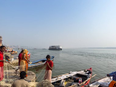Varanasi, Uttar Pradesh, Hindistan - 18 Kasım 2022: Varanasi 'deki nehir çetelerinin yakınındaki ghat' larda bir grup insanla ahşap botlar.