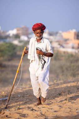 Puşkar, Rajasthan, Hindistan - 1 Kasım 2024: Çöldeki fuar alanında deve ticareti sırasında geleneksel giysiler içinde bir rajasthani erkeğinin portresi.