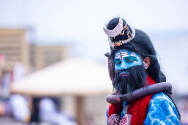 Varanasi, Uttar Pradesh, India - March 21, 2024: Portrait of a young boy dressed like lord shiv with painted face walking on the ghat of river ganga during winter morning in varanasi.