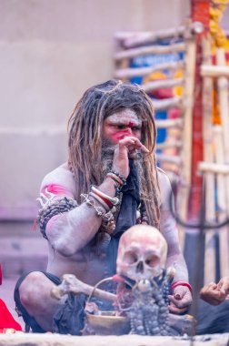 Varanasi, Uttar Pradesh, India - March 21, 2024: Masan Holi, Portrait of an unidentified aghori sadhu smoking and performing rituals during masan holi festival in varanasi at harishchandra ghat.