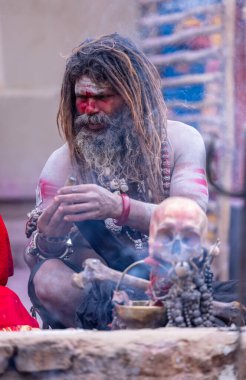 Varanasi, Uttar Pradesh, India - March 21, 2024: Masan Holi, Portrait of an unidentified aghori sadhu smoking and performing rituals during masan holi festival in varanasi at harishchandra ghat.