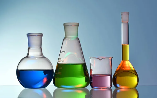 蓝色背景上含有五颜六色液体和化学物质的实验室玻璃器皿 — 图库照片