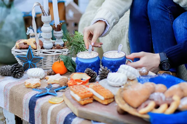 Winter decor sweet table. Mugs with cocoa. People hands