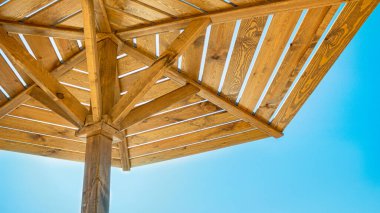  Sahilde mavi arka planda bir güneş şemsiyesi. Masmavi güneşli gökyüzüne karşı ahşap plaj şemsiyeleri