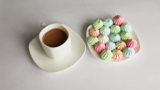 Veelkleurige meringues en een kop koffie op een witte achtergrond. geïsoleerd — Stockvideo